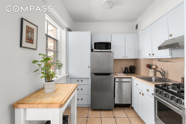 kitchen featuring a sink, decorative backsplash, light countertops, under cabinet range hood, and appliances with stainless steel finishes