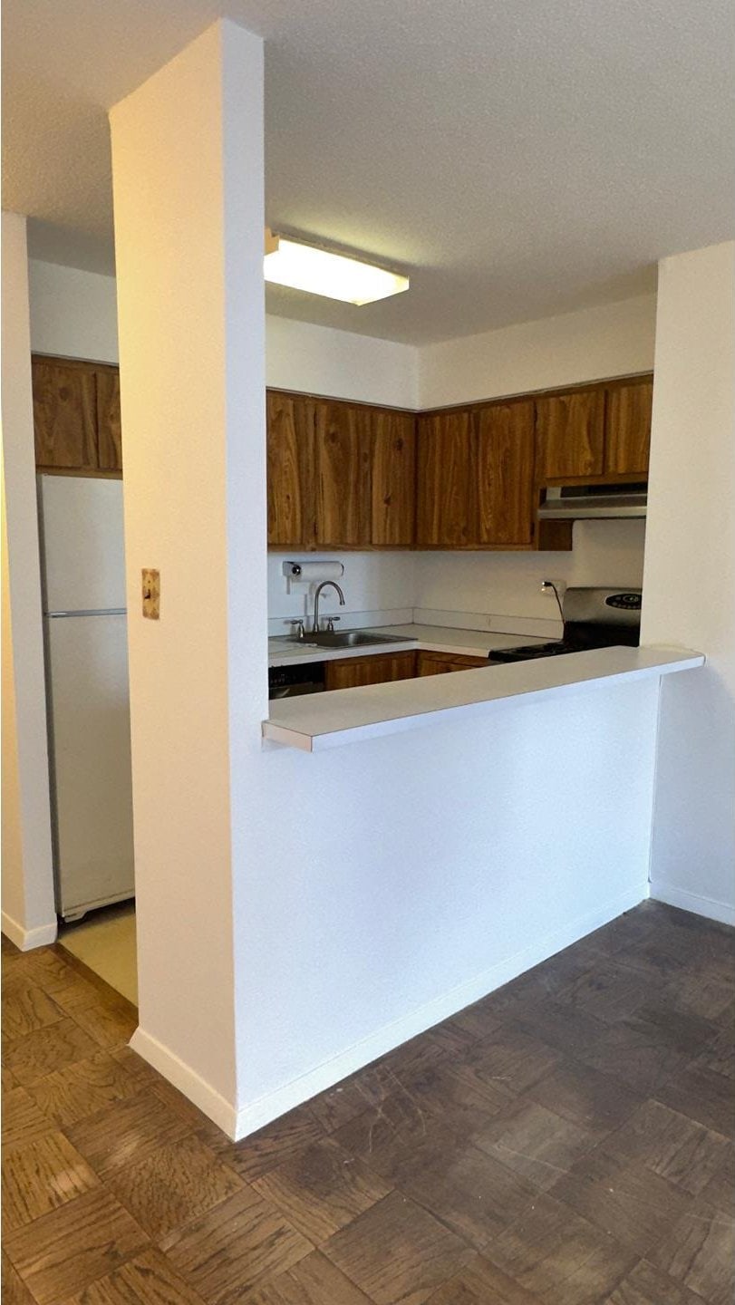 kitchen with brown cabinets, under cabinet range hood, a sink, freestanding refrigerator, and range