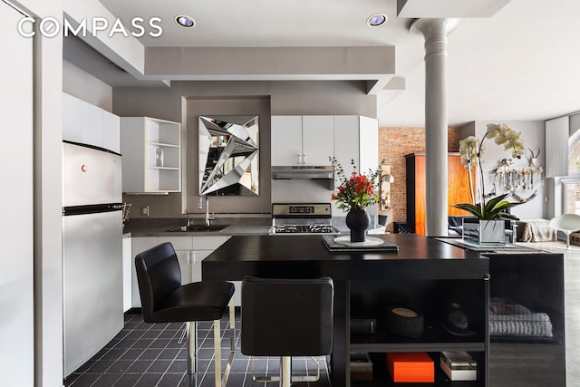 kitchen featuring range with gas stovetop, decorative columns, freestanding refrigerator, a sink, and under cabinet range hood