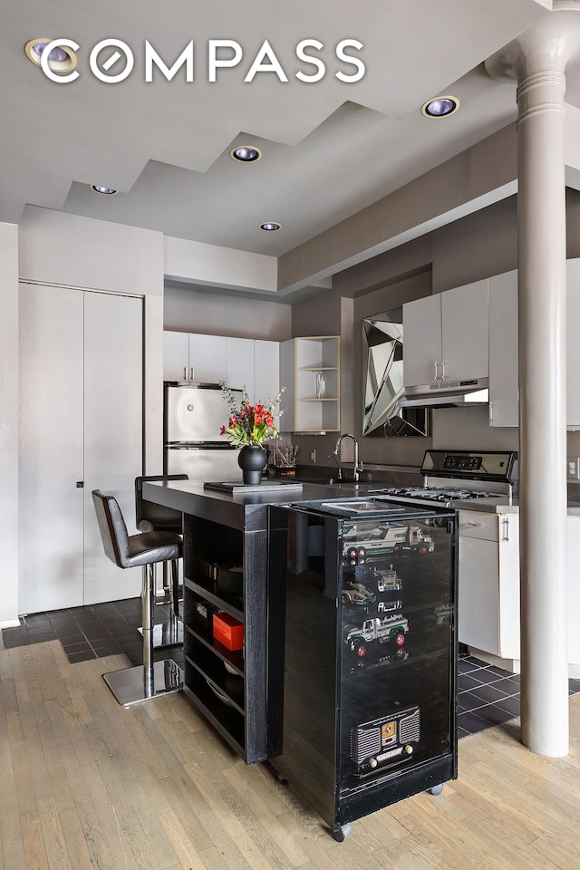 kitchen with open shelves, light wood-style floors, dark countertops, and ornate columns