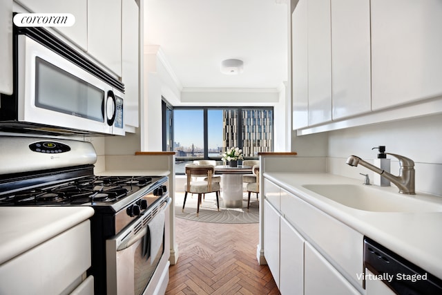 kitchen with a sink, stainless steel gas range, ornamental molding, and white cabinets