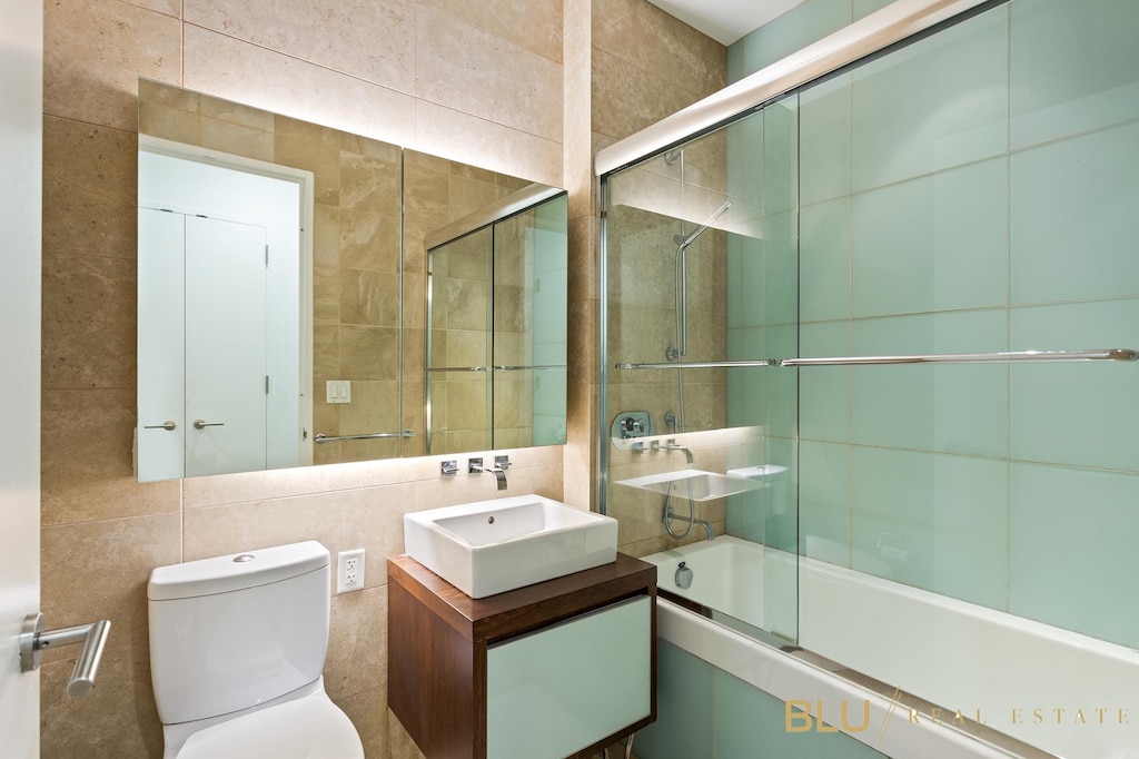 full bath featuring vanity, decorative backsplash, tile walls, toilet, and combined bath / shower with glass door