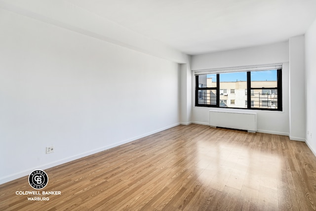 empty room with baseboards, wood finished floors, and radiator heating unit