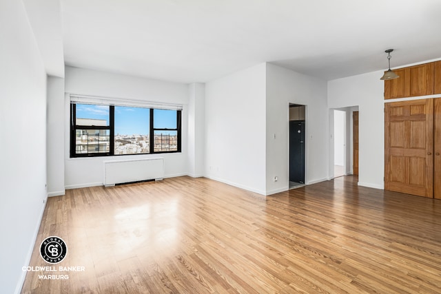 unfurnished living room featuring light wood-style floors, radiator, and baseboards