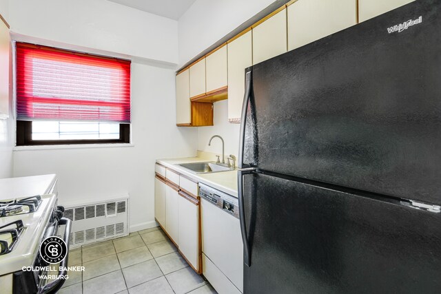 kitchen featuring a sink, white appliances, light countertops, radiator heating unit, and light tile patterned floors