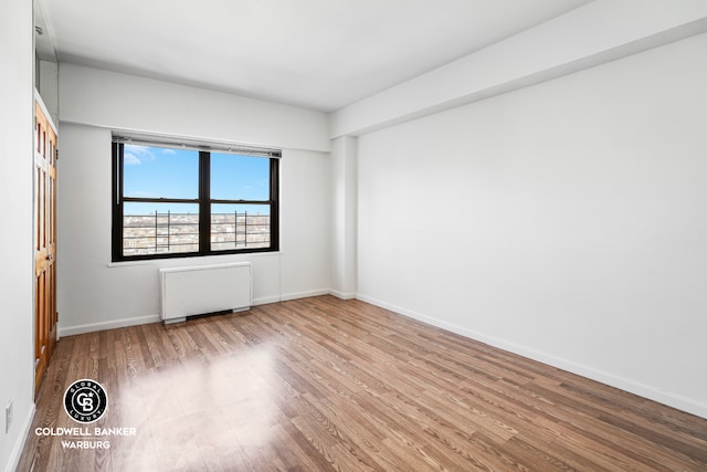 unfurnished room featuring baseboards, wood finished floors, and radiator heating unit