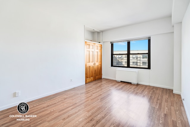 empty room featuring baseboards, radiator heating unit, and wood finished floors