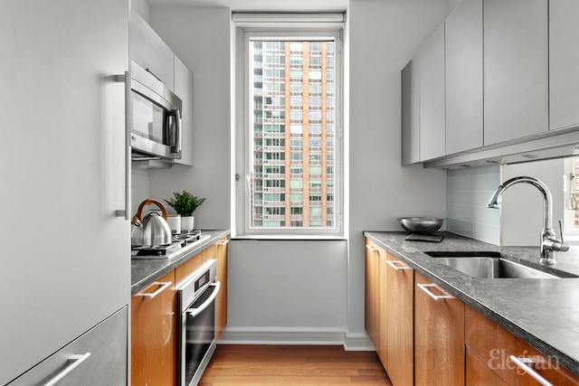 kitchen featuring brown cabinetry, baseboards, light wood-style flooring, a sink, and stainless steel appliances