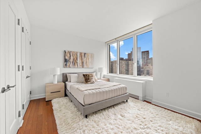 bedroom featuring a view of city, baseboards, and wood-type flooring