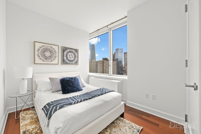 bedroom with a view of city, baseboards, and wood finished floors