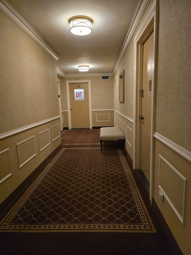 corridor with a decorative wall, dark carpet, and ornamental molding