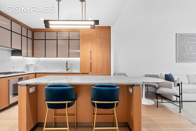 kitchen featuring oven, a sink, tasteful backsplash, a breakfast bar area, and stainless steel gas cooktop