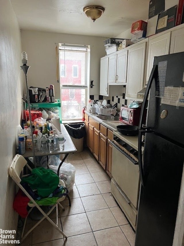 kitchen with light tile patterned flooring, freestanding refrigerator, light countertops, range, and brown cabinets