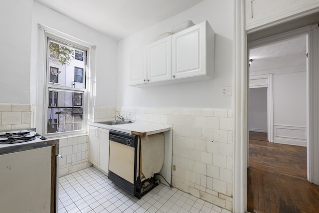 kitchen featuring tile walls, dishwasher, wainscoting, white cabinetry, and a sink