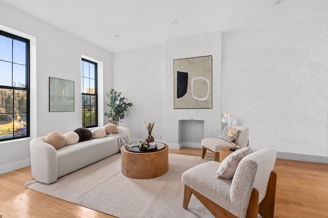 living room with a brick fireplace, wood finished floors, baseboards, and brick wall