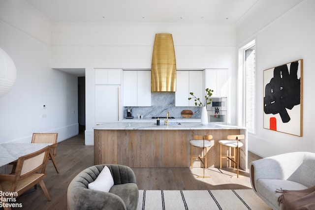 kitchen with light stone countertops, a breakfast bar area, decorative backsplash, wood finished floors, and white cabinets