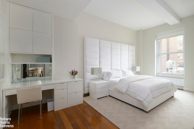 bedroom with beam ceiling, wood finished floors, and built in desk