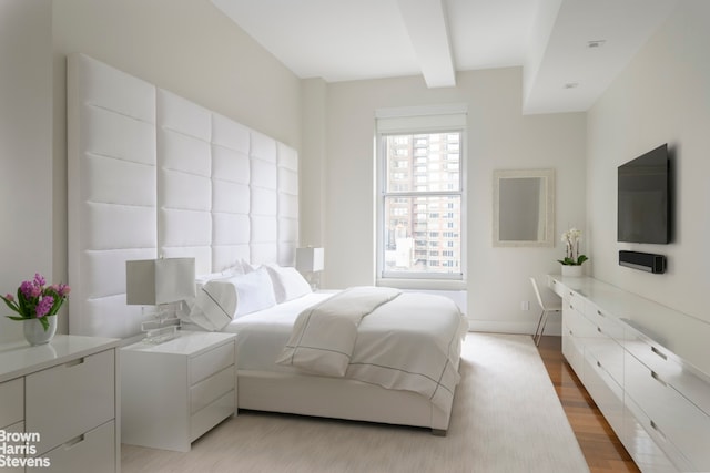 bedroom with light wood-type flooring, beam ceiling, and baseboards