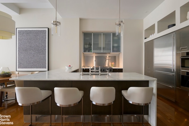 kitchen with light stone counters, dark wood-style floors, a sink, a kitchen breakfast bar, and decorative light fixtures