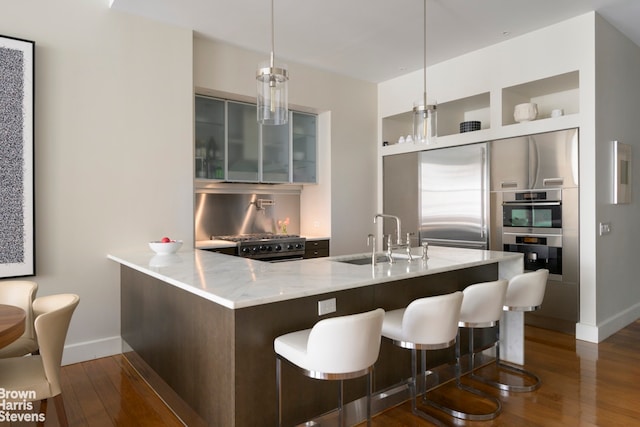 kitchen featuring dark wood-style floors, light stone countertops, stainless steel appliances, a sink, and glass insert cabinets