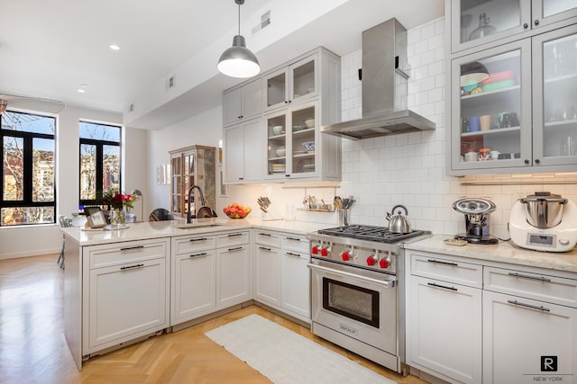 kitchen with tasteful backsplash, wall chimney range hood, premium stove, a peninsula, and a sink