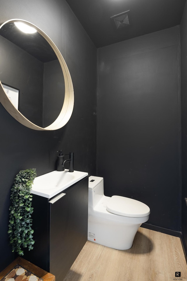 half bathroom featuring a sink, visible vents, toilet, and wood finished floors