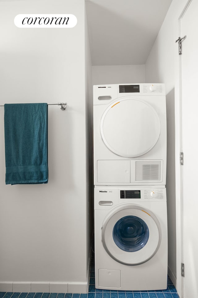 clothes washing area featuring tile patterned flooring, laundry area, baseboards, and stacked washing maching and dryer