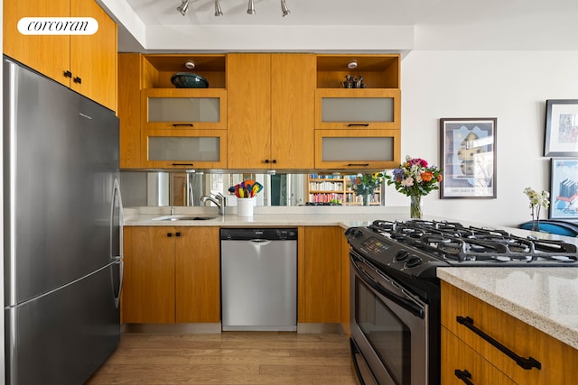 kitchen with open shelves, light wood-type flooring, light stone counters, appliances with stainless steel finishes, and a sink