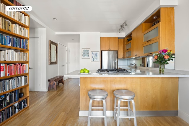 kitchen featuring light countertops, appliances with stainless steel finishes, a peninsula, light wood-style floors, and brown cabinetry