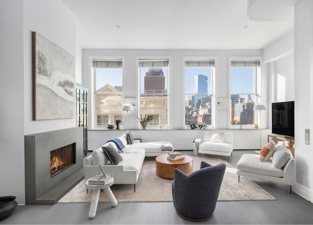 living area with baseboards, a lit fireplace, and wood finished floors