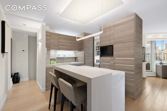 kitchen featuring light wood-type flooring, modern cabinets, a breakfast bar, a kitchen island, and light countertops