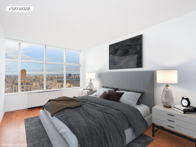 bedroom featuring wood finished floors, a view of city, radiator heating unit, and visible vents