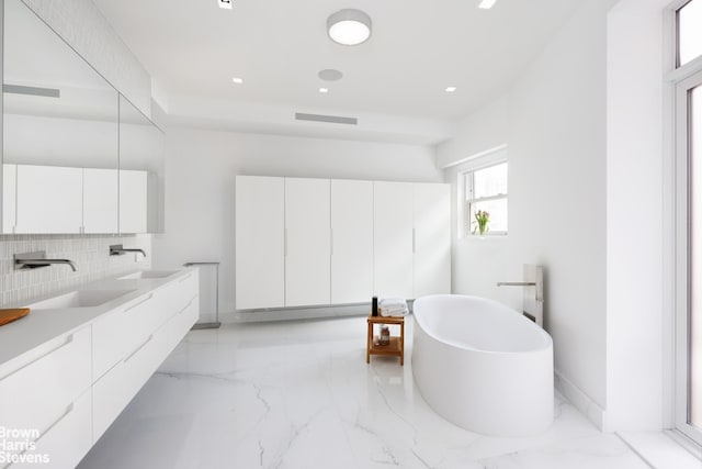 bathroom featuring visible vents, a freestanding bath, decorative backsplash, and a sink