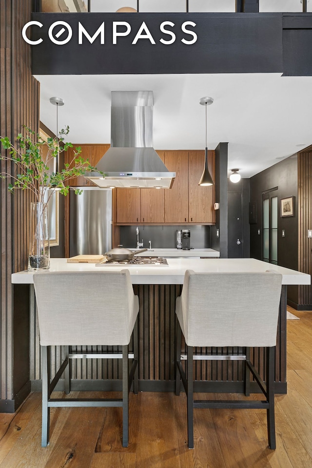 kitchen featuring brown cabinetry, light wood-style flooring, light countertops, and island range hood