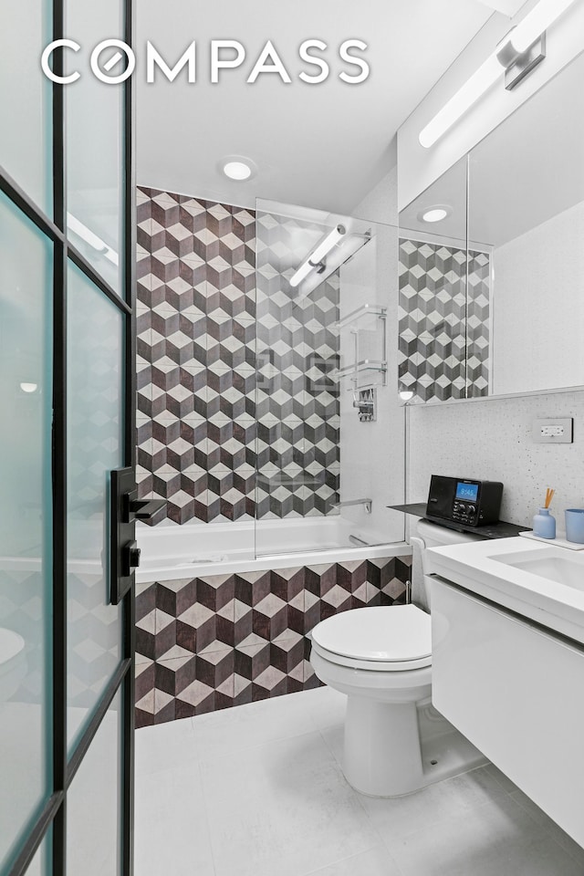 bathroom featuring tile patterned flooring, tile walls, toilet, tiled shower / bath combo, and vanity