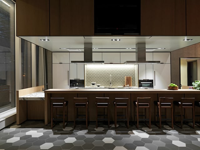 kitchen with oven, a kitchen bar, ventilation hood, white cabinets, and light countertops