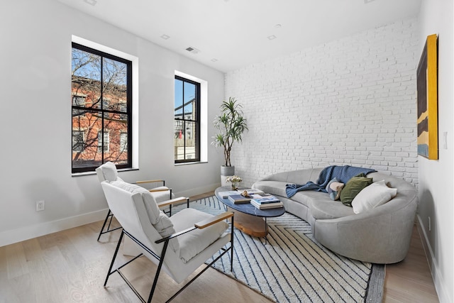 living area with light wood-style flooring, baseboards, visible vents, and brick wall