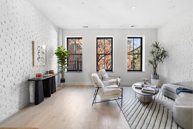 living area with visible vents, baseboards, light wood-style floors, and brick wall