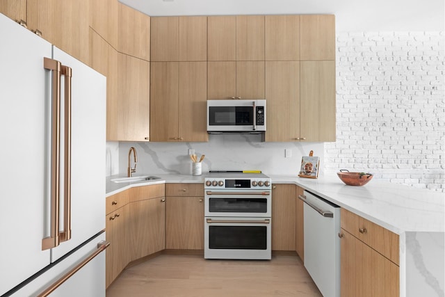 kitchen featuring tasteful backsplash, light stone counters, light wood-style flooring, white appliances, and a sink