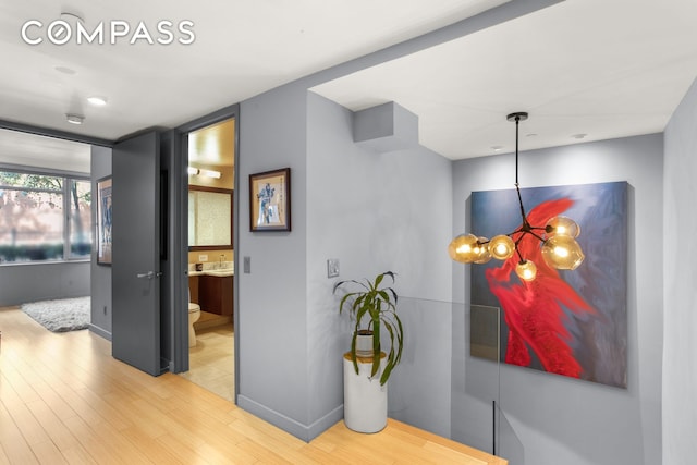 hall with wood finished floors, baseboards, and a chandelier