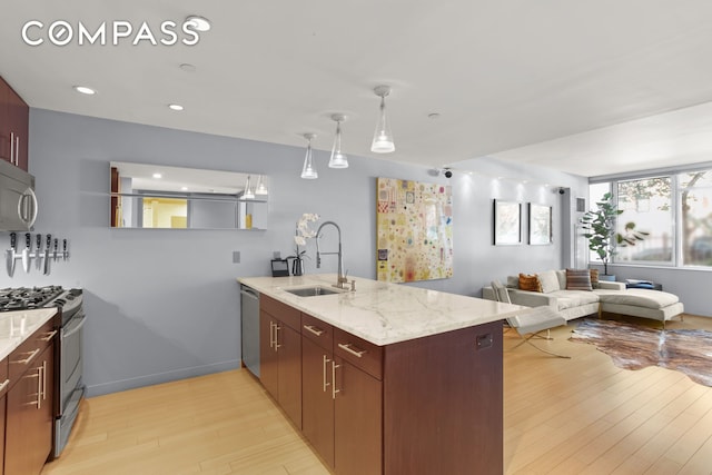 kitchen featuring a sink, stainless steel appliances, a peninsula, light wood finished floors, and light stone counters