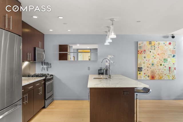 kitchen featuring stainless steel appliances, a sink, light wood-type flooring, recessed lighting, and dark brown cabinets