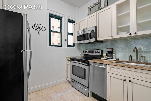 kitchen with light tile patterned floors, light stone countertops, a sink, stainless steel appliances, and tasteful backsplash