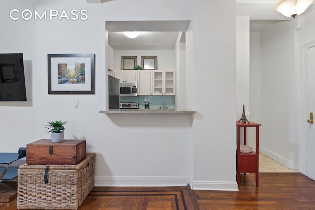 kitchen featuring stainless steel microwave, tasteful backsplash, refrigerator, white cabinetry, and glass insert cabinets