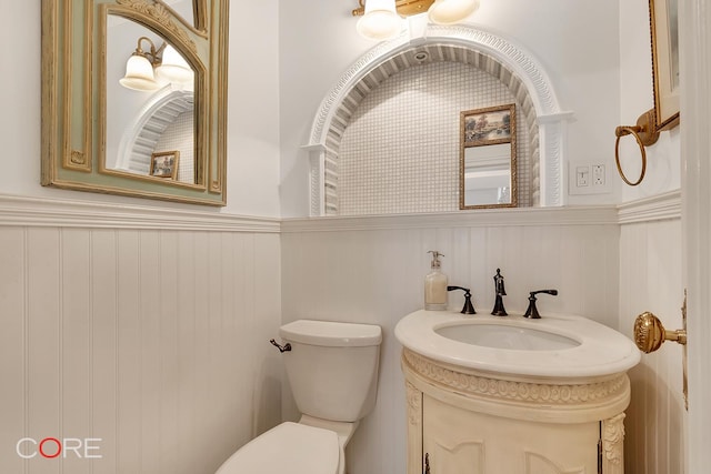 bathroom featuring vanity, toilet, and a wainscoted wall