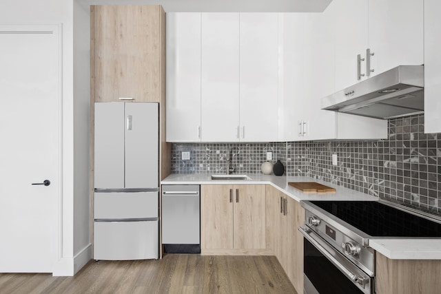 kitchen with appliances with stainless steel finishes, extractor fan, a sink, wood finished floors, and light countertops