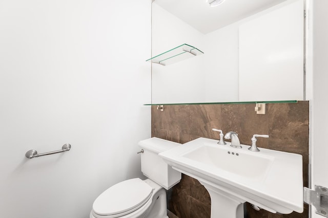 half bath with tile walls, toilet, tasteful backsplash, and a sink