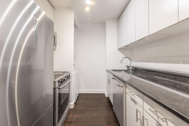 kitchen with tasteful backsplash, dark stone countertops, white cabinets, stainless steel appliances, and a sink