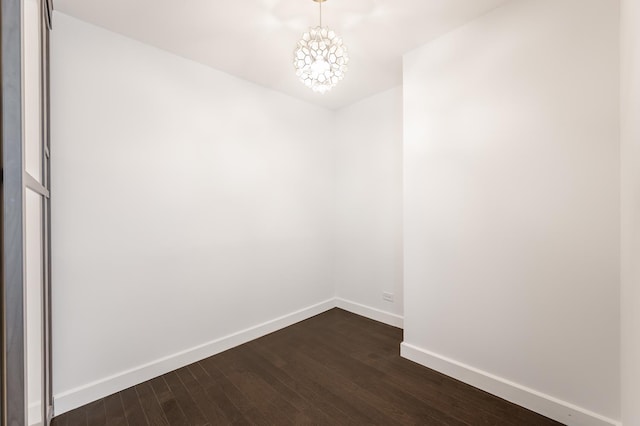 empty room with a notable chandelier, baseboards, and dark wood-style flooring