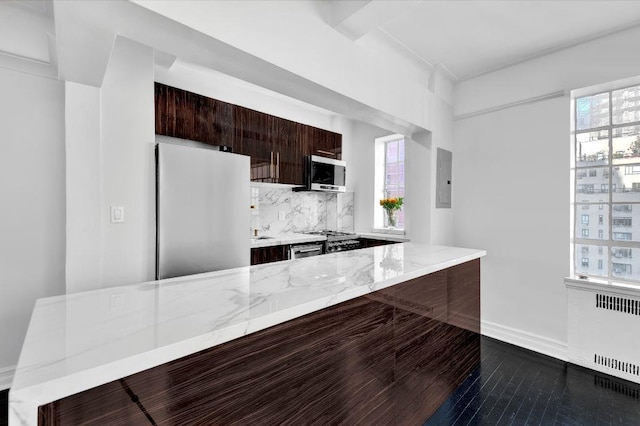 kitchen with freestanding refrigerator, stainless steel microwave, modern cabinets, radiator heating unit, and backsplash
